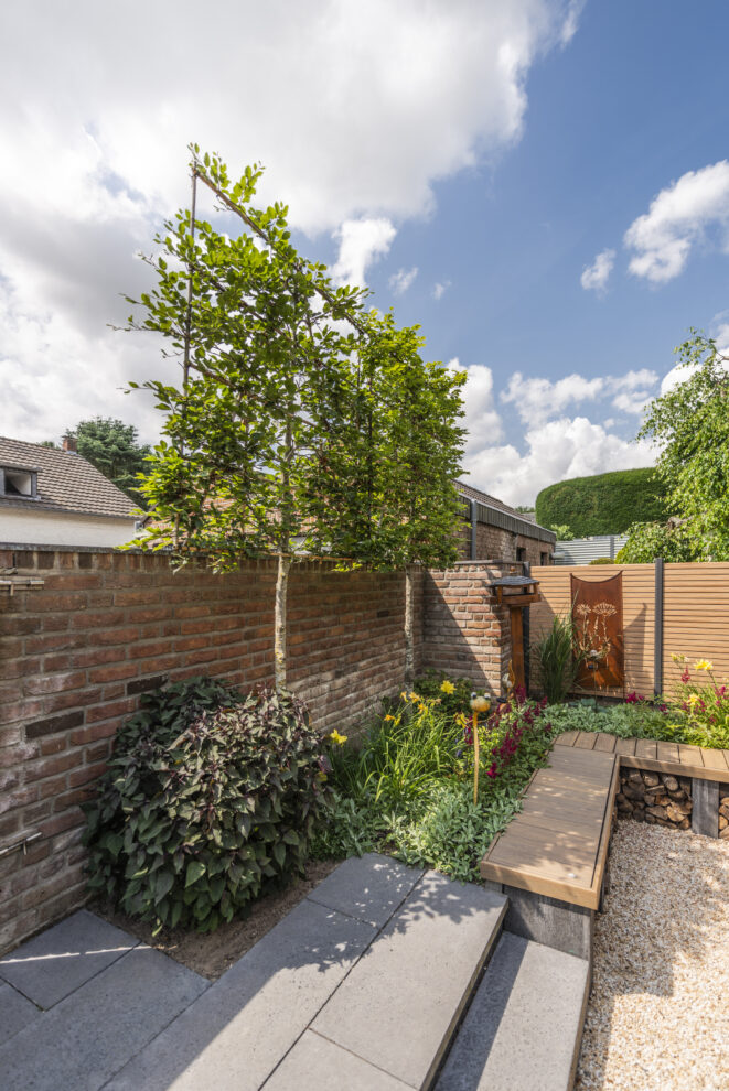 Bepflanzter Garten mit Blühstauden vor einer Backsteinmauer.