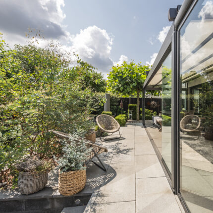 Terrasse mit Korbsesseln und Pflanzkübeln, umgeben von üppiger Vegetation.