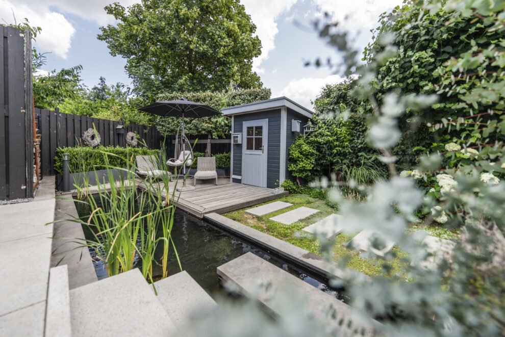 Gemütlicher Loungebereich neben dem Gartenteich, eingerahmt von Pflanzen.