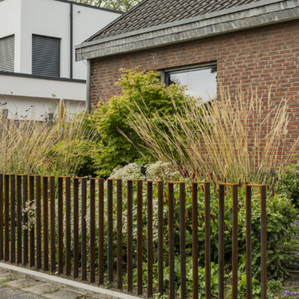 Vorgarten gestalten mit Cortenstahl-Stabzaun und Ziergräsern vor Klinkerbungalow