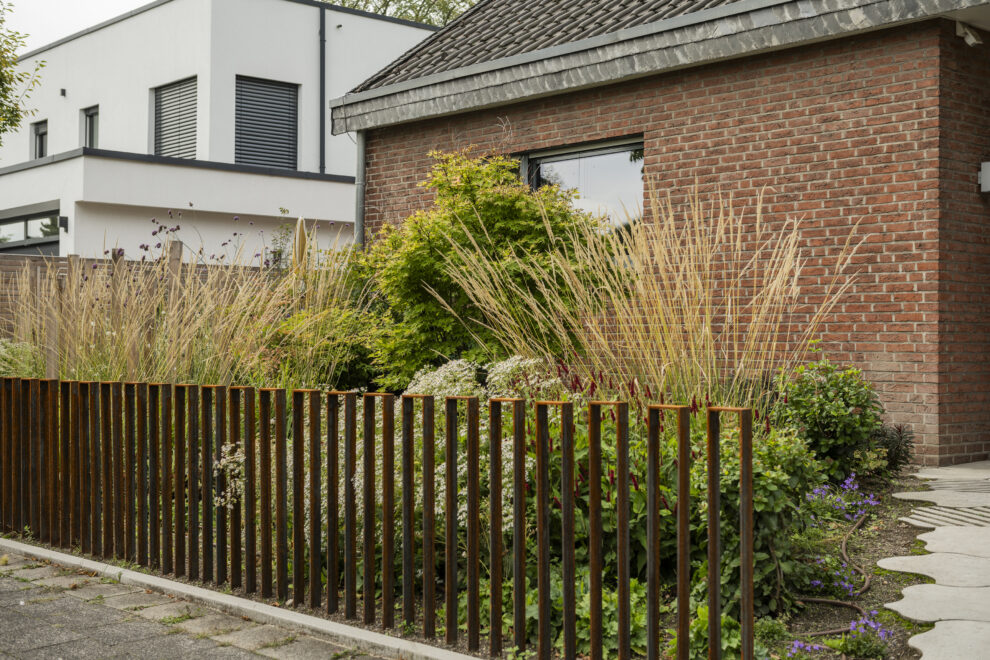 Vorgarten gestalten mit Cortenstahl-Stabzaun und Ziergräsern vor Klinkerbungalow