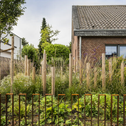 Vorgarten mit Holzpfählen, Gräsern und Cortenstahl-Zaun am Klinkerbungalow