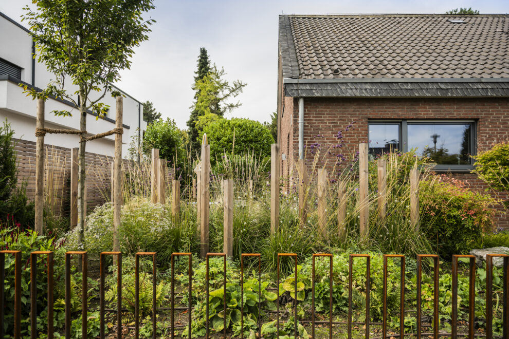 Vorgarten mit Holzpfählen, Gräsern und Cortenstahl-Zaun am Klinkerbungalow