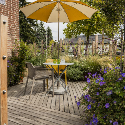 Holzterrasse mit Sitzplatz und Sonnenschirm zwischen Stauden und Gräsern