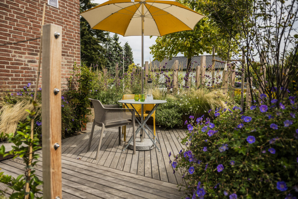 Holzterrasse mit Sitzplatz und Sonnenschirm zwischen Stauden und Gräsern